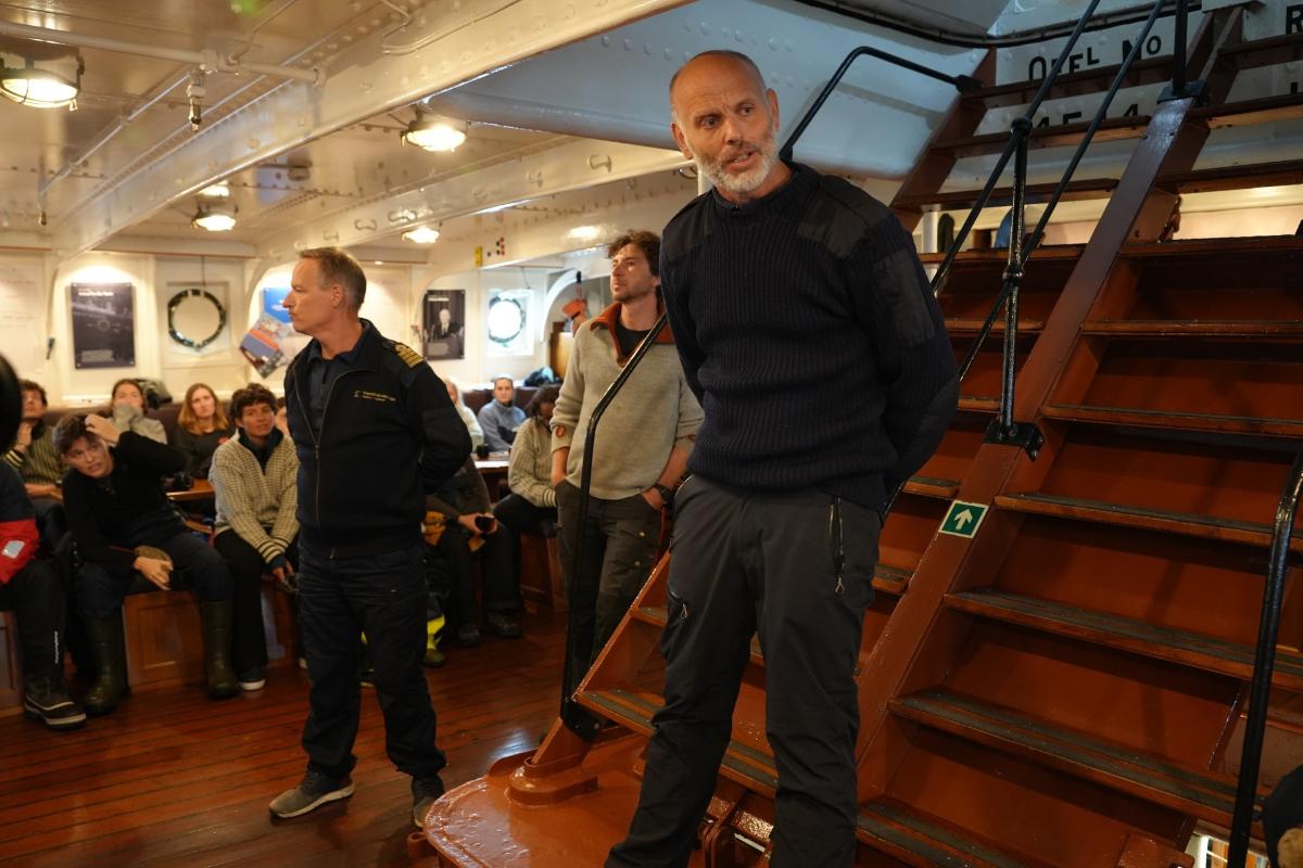 ekspedisjonsleder Maxime Geoffroy og kaptein Marcus Zeidl og Haakon Vatle.jpg en mann i står ved en trapp og snakker itil en gruppe mennesker